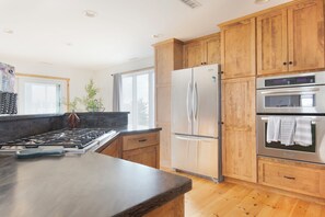 A modern kitchen with wooden cabinets, stainless steel appliances, a granite countertop, and a window providing natural light. - Private, serene house 5-min to beach with panoramic views from two decks (Milford)