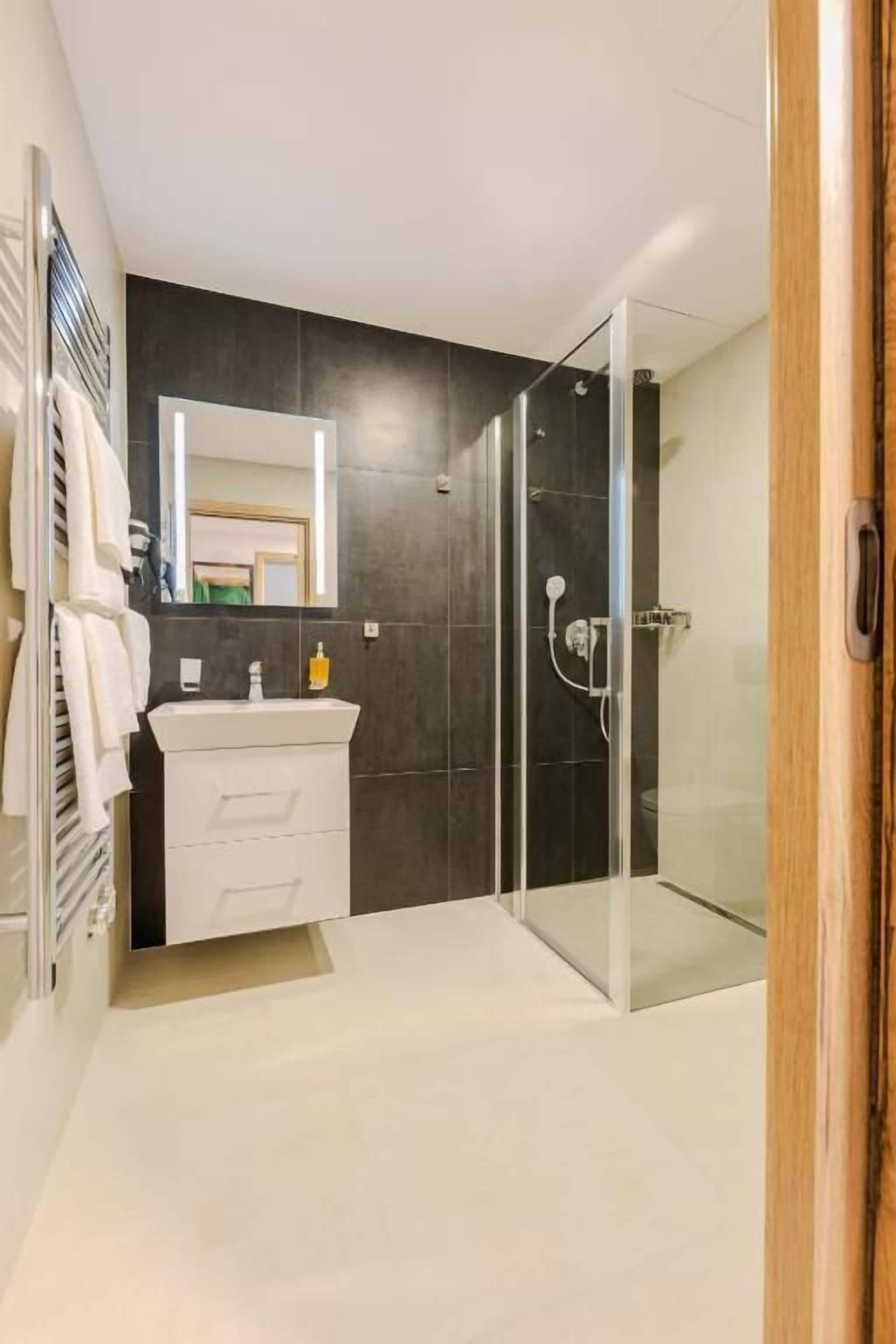 A modern bathroom with a glass shower enclosure, a white vanity, and a large mirror.