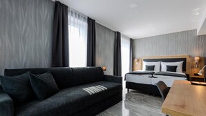Quarto de hotel moderno com sofá escuro, cama com cabeceira de madeira, escrivaninha de madeira e chão de mármore.