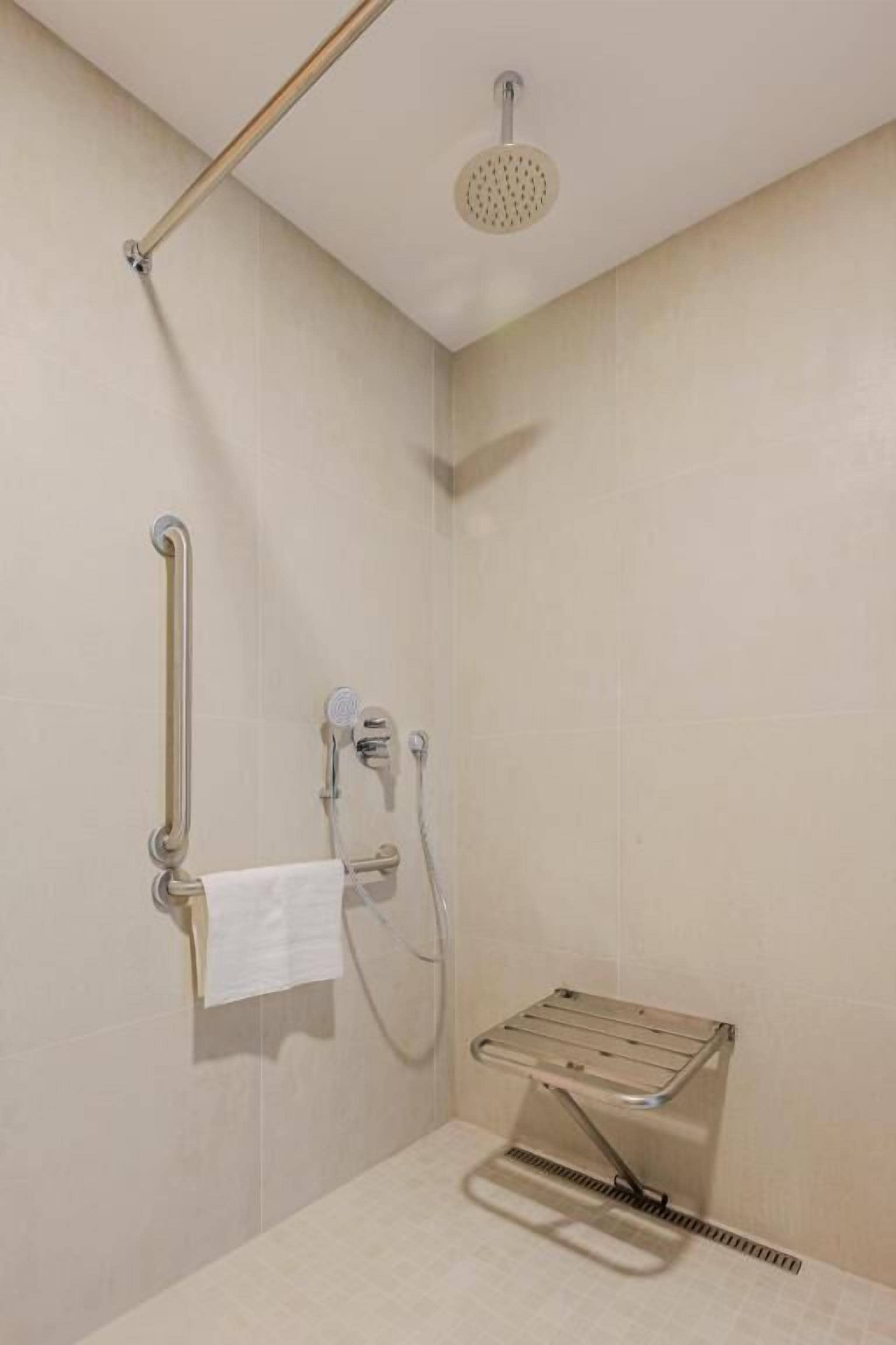 Un área de ducha con cabezal de ducha manual, control de ducha manual, toallero con toalla y asiento de ducha.