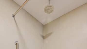 Un área de ducha con cabezal de ducha manual, control de ducha manual, toallero con toalla y asiento de ducha.