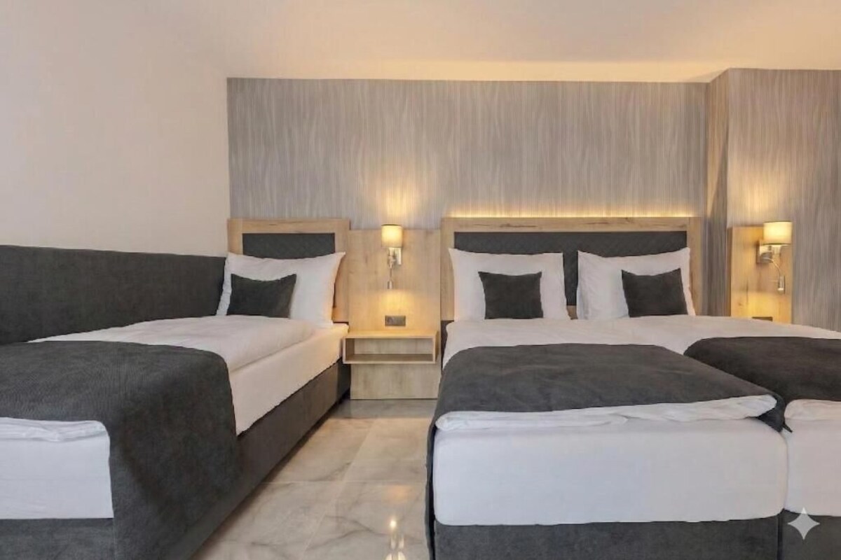 A hotel room with two beds, each with a headboard, bedside tables, and wall-mounted lamps.