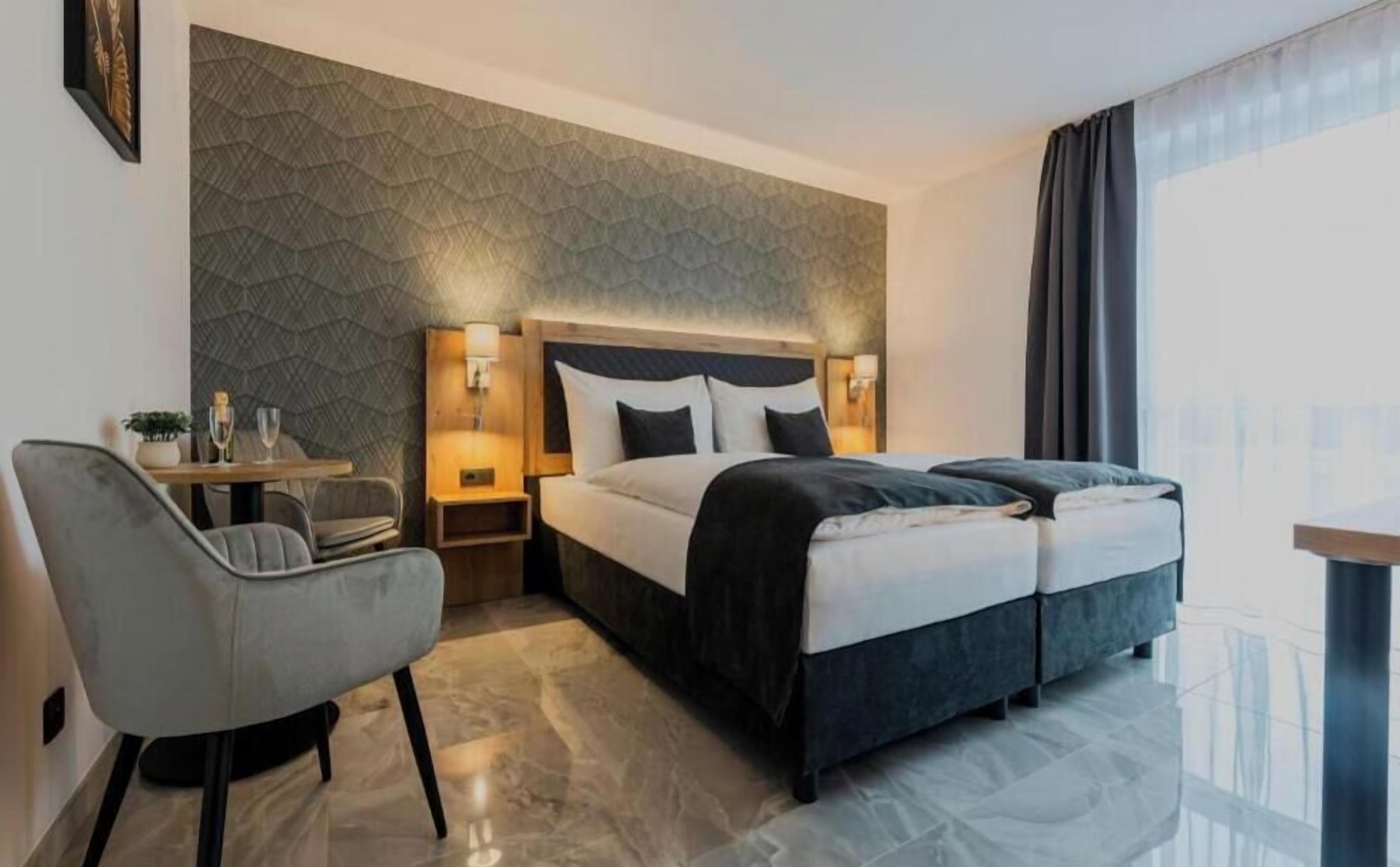 A hotel room with a bed, bedside tables, a chair, and a view of the city.