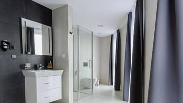 Un baño moderno con tocador blanco, cabina de ducha de vidrio y un espejo grande.