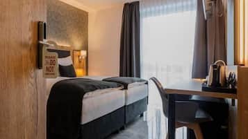 Habitación de hotel con cama, escritorio, silla, ventana con cortinas y puerta.