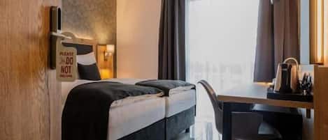 A hotel room with a bed, a desk, a chair, a window with curtains, and a door.