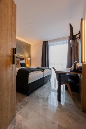 A hotel room with a bed, a desk, a chair, a window with curtains, and a door. - Hotel Tříška (Brandys nad Labem-Stara Boleslav)