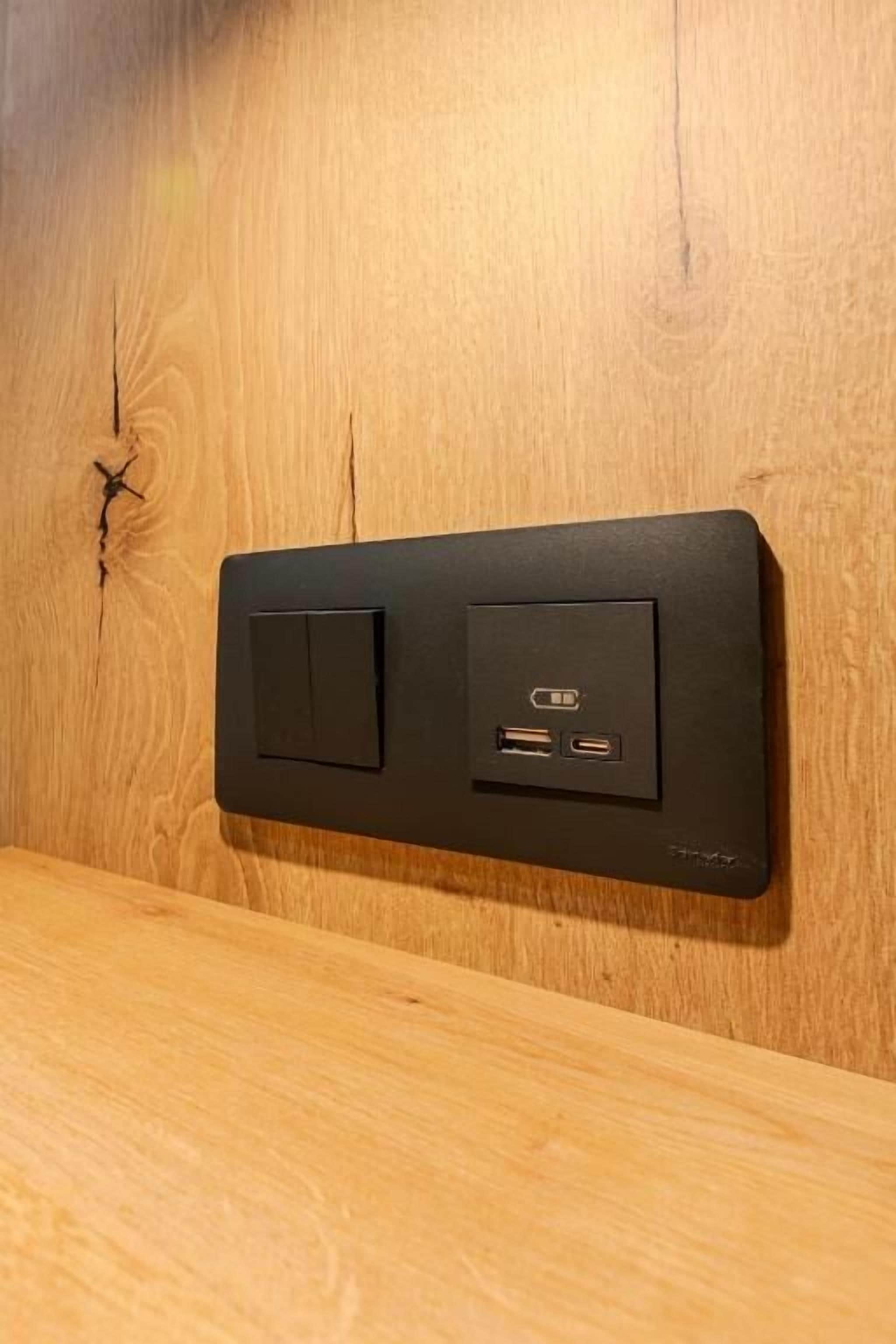 Un tablero de interruptores negro montado en la pared con dos interruptores y dos puertos USB.