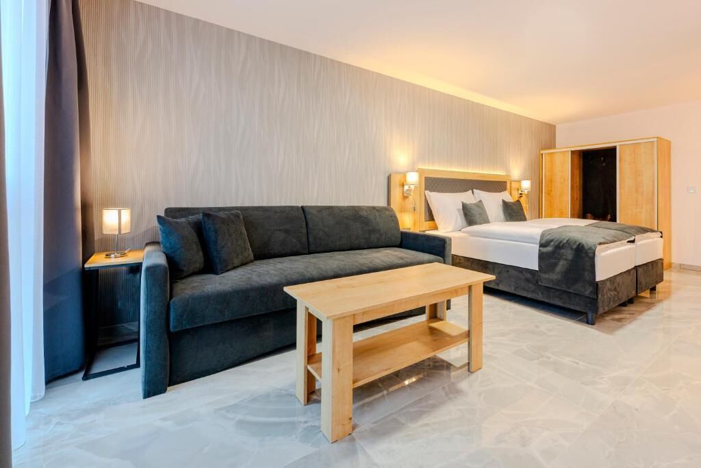 Habitación de hotel con sofá, cama, mesa de madera y mesita de noche con lámpara.