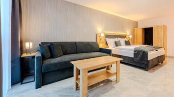 Habitación de hotel con sofá, cama, mesa de madera y mesita de noche con lámpara.