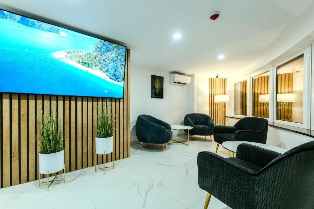A modern hotel lobby with a large TV screen displaying a scenic view, comfortable seating, and a wooden accent wall.