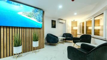 A modern hotel lobby with a large TV screen displaying a scenic view, comfortable seating, and a wooden accent wall.