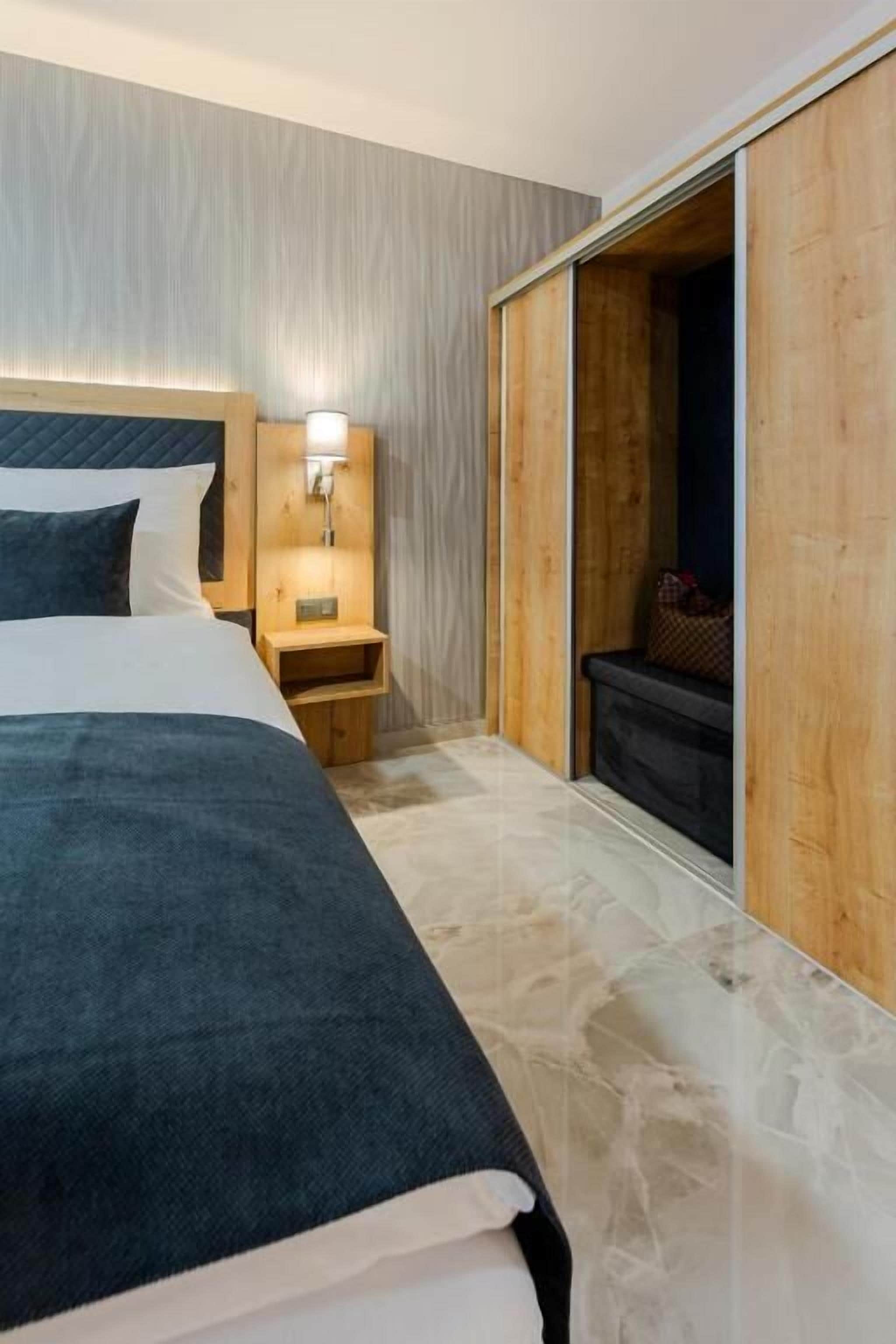 A hotel room with a bed, a nightstand, a wall-mounted lamp, and a sliding door leading to a bathroom.
