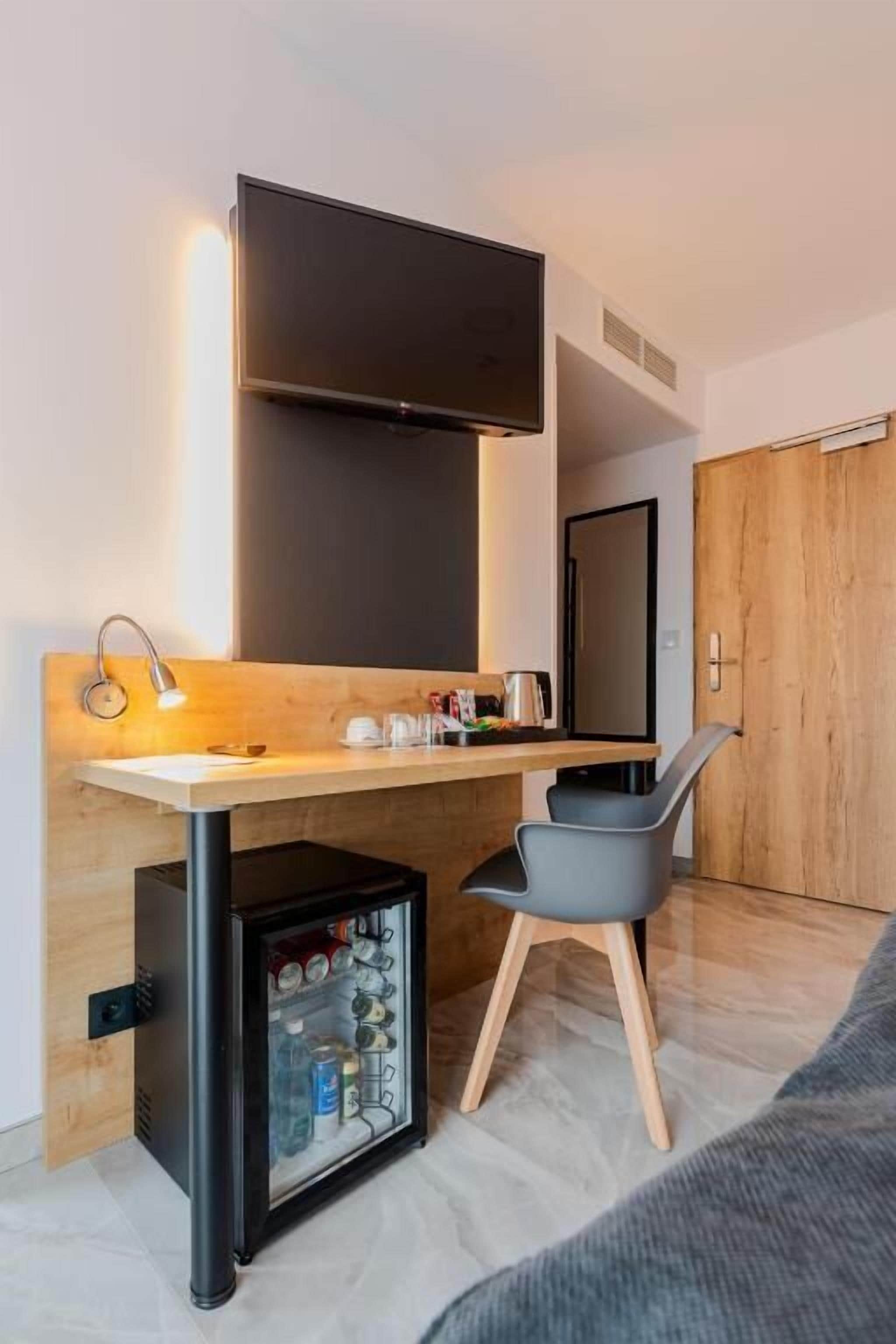 Una habitación compacta con escritorio, una silla, refrigerador pequeño y televisión montada en la pared.