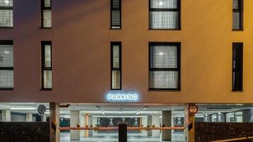 Un edificio con letrero 'PARKING', múltiples ventanas y una entrada cubierta a un estacionamiento.