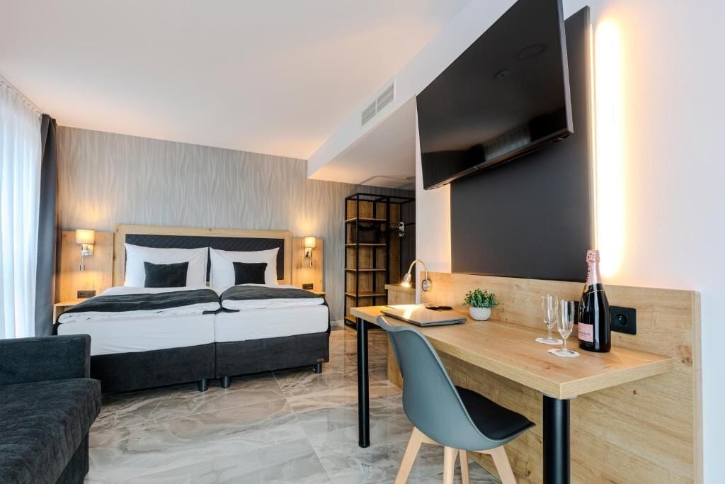 A modern hotel room with a bed, desk, chair, and a flat-screen TV mounted on the wall.