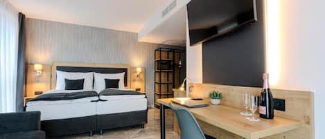 A modern hotel room with a bed, desk, chair, and a flat-screen TV mounted on the wall.