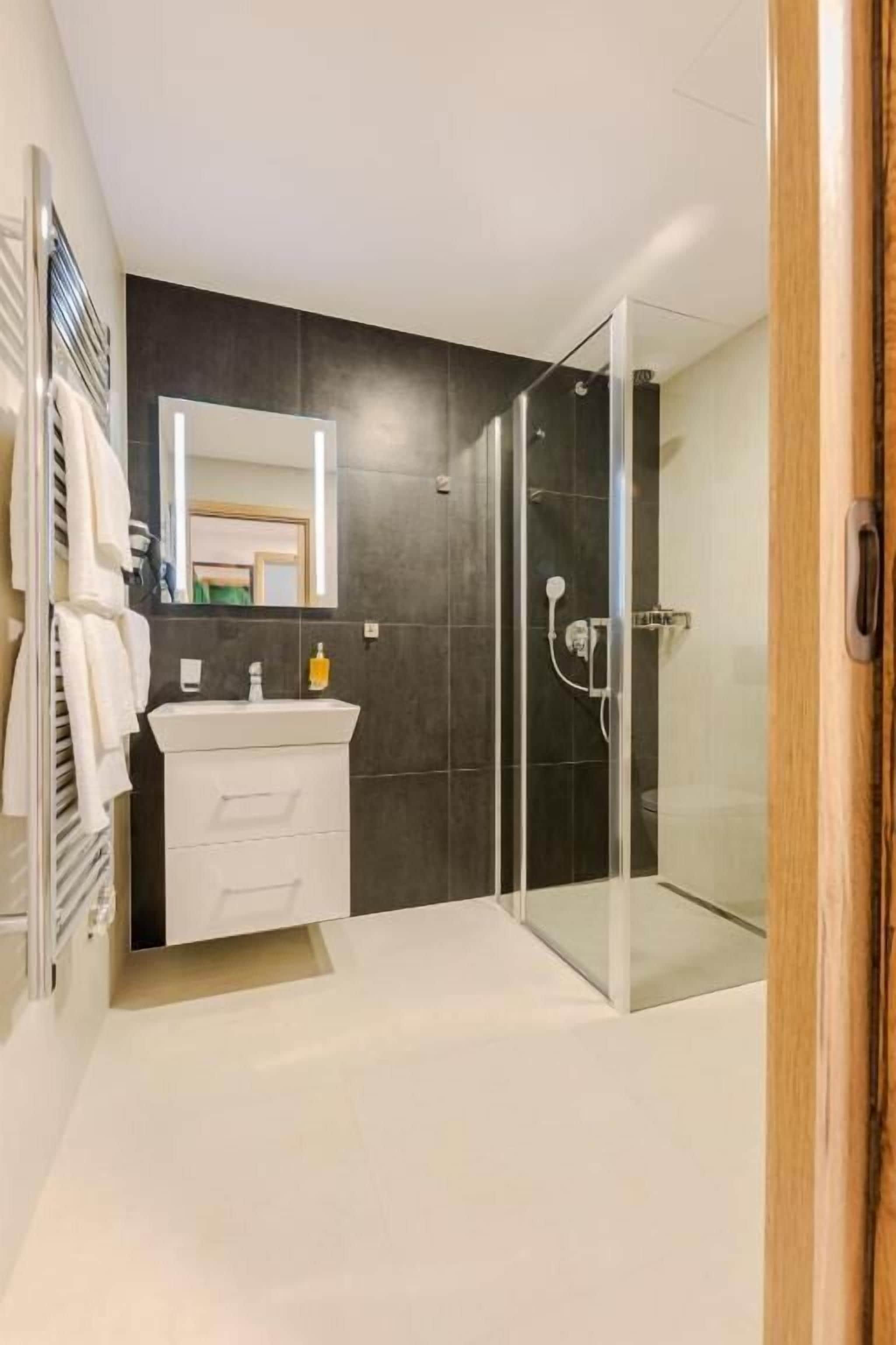Une salle de bain moderne avec une douche à parois de verre, un meuble-lavabo blanc et un grand miroir.