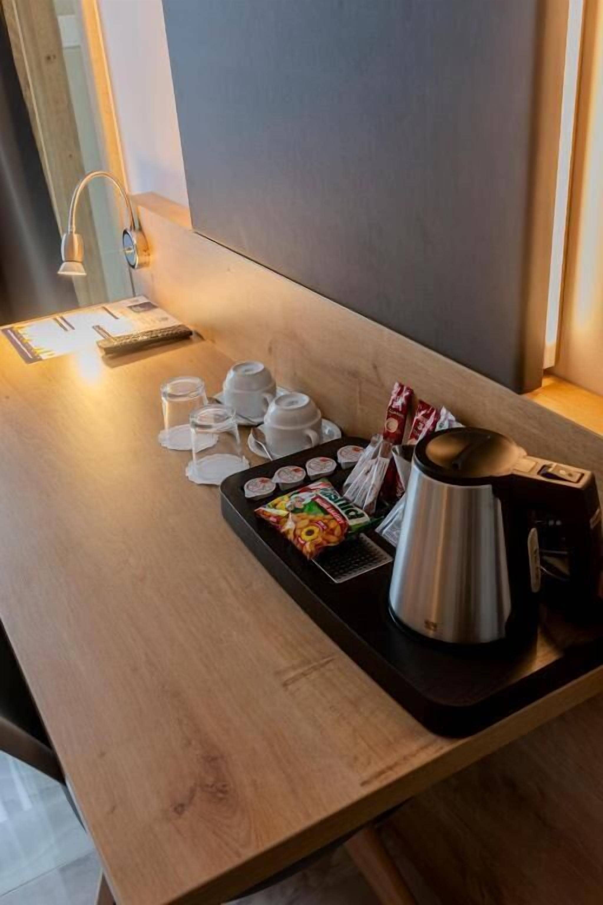 A wooden table with a tray containing a teapot, cups, and packaged snacks.