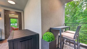 En balkon med træterrasse, et bord med en stol og en potteplante.