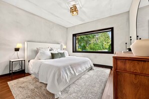 A bedroom with a bed, bedside tables, a window with a view of greenery, and a wooden dresser. - The Perch | Rooftop Putting Green Retreat (Tracy City)