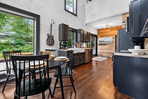 A modern kitchen with a dining area, large windows, and a guitar on the wall. - The Perch | Rooftop Putting Green Retreat (Tracy City)