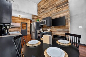A modern kitchen with wooden panel walls, stainless steel appliances, and a dining area with black tables and woven placemats. - The Perch | Luxury TH + Rooftop Retreat in Nature (Tracy City)