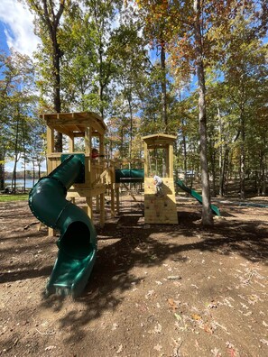 A playground with a slide and climbing structures, surrounded by trees and a dirt ground. - The Perch | Rooftop Putting Green Retreat (Tracy City)