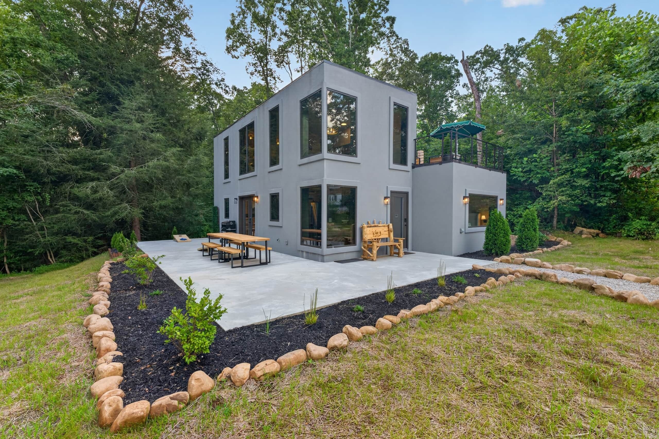 Ein modernes, zweistöckiges Haus mit einer Terrassenfläche, Sitzgelegenheiten im Freien und einem Garten.