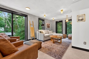 A modern living room with a sofa, a coffee table, and a view of greenery through large windows. - The Perch | Luxury TH + Rooftop Retreat in Nature (Tracy City)