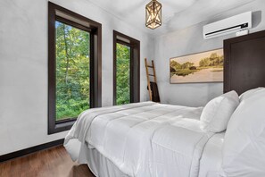 A bedroom with a large bed, two windows, a painting, an air conditioning unit, and a wooden ladder. - The Prominence | Double Rooftop Lounge + Outdoor Movie (Tracy City)