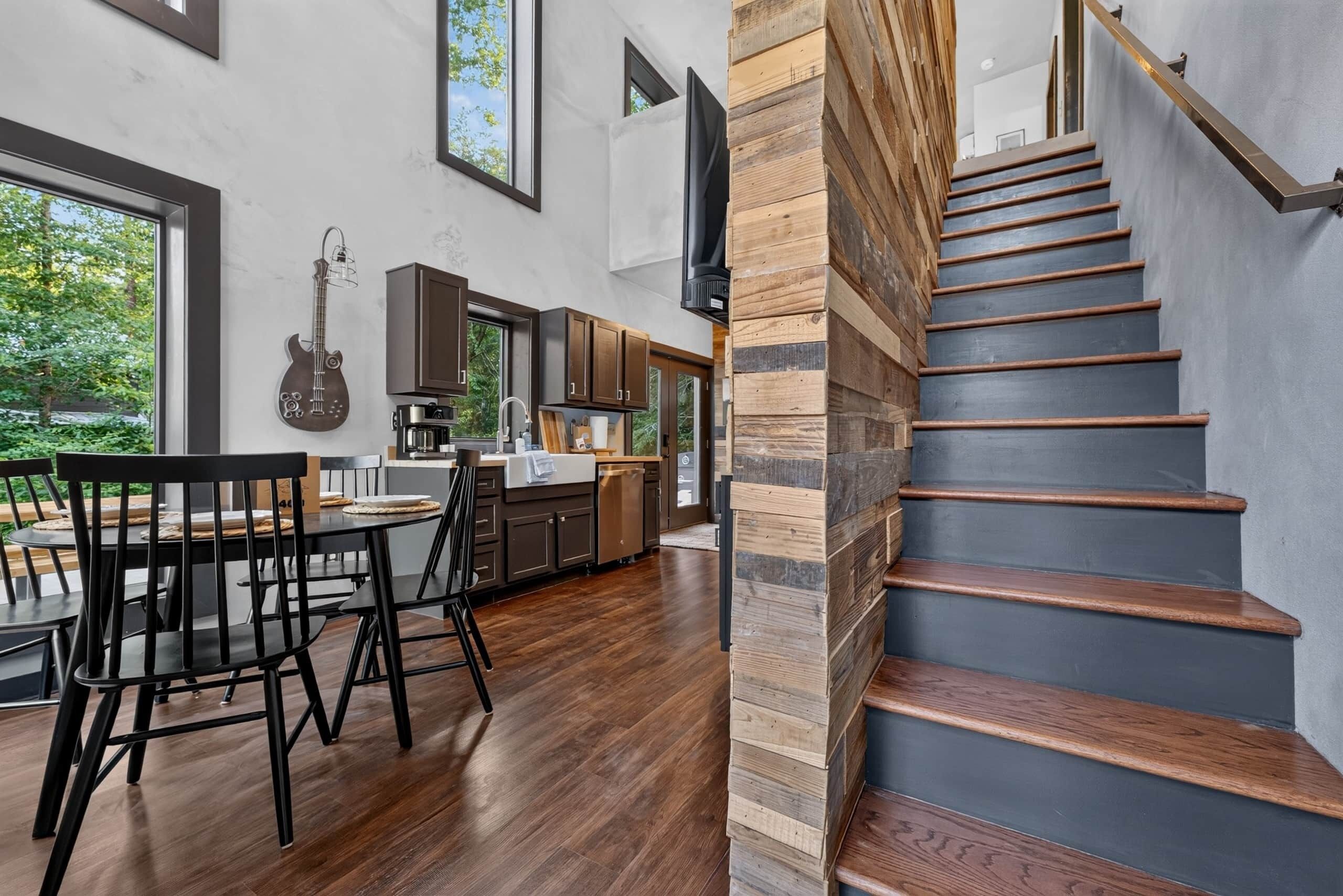 A modern kitchen with dark wooden cabinets, a dining area with a table and chairs, and a staircase with wooden steps.