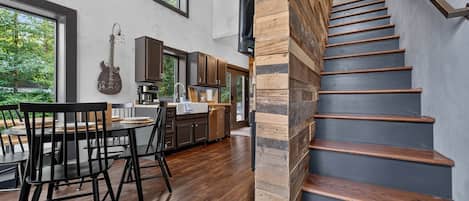 A modern kitchen with dark wooden cabinets, a dining area with a table and chairs, and a staircase with wooden steps.