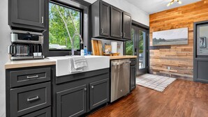 A modern kitchen with dark cabinetry, a built-in dishwasher, and a window overlooking greenery. - The Prominence | Luxury TH + Double Rooftop Lounge (Tracy City)