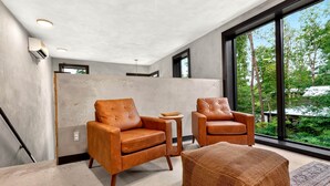 A modern living room with two leather armchairs, a small side table, and a large window offering a view of trees. - The Prominence | Luxury TH + Double Rooftop Lounge (Tracy City)