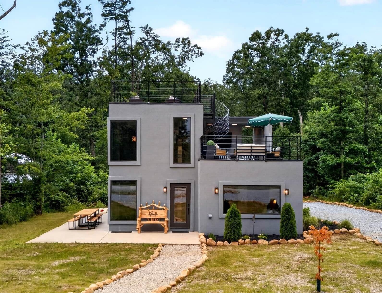 A modern two-story house with a balcony, a spiral staircase, and a small outdoor seating area.