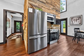 A modern kitchen with stainless steel appliances, wooden wall paneling, and a large window. - The Prominence | Double Rooftop Lounge + Outdoor Movie (Tracy City)