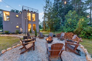 A modern outdoor seating area with Adirondack chairs and a fire pit, surrounded by a gravel path and a wooden deck. - The Prominence | Double Rooftop Lounge + Outdoor Movie (Tracy City)