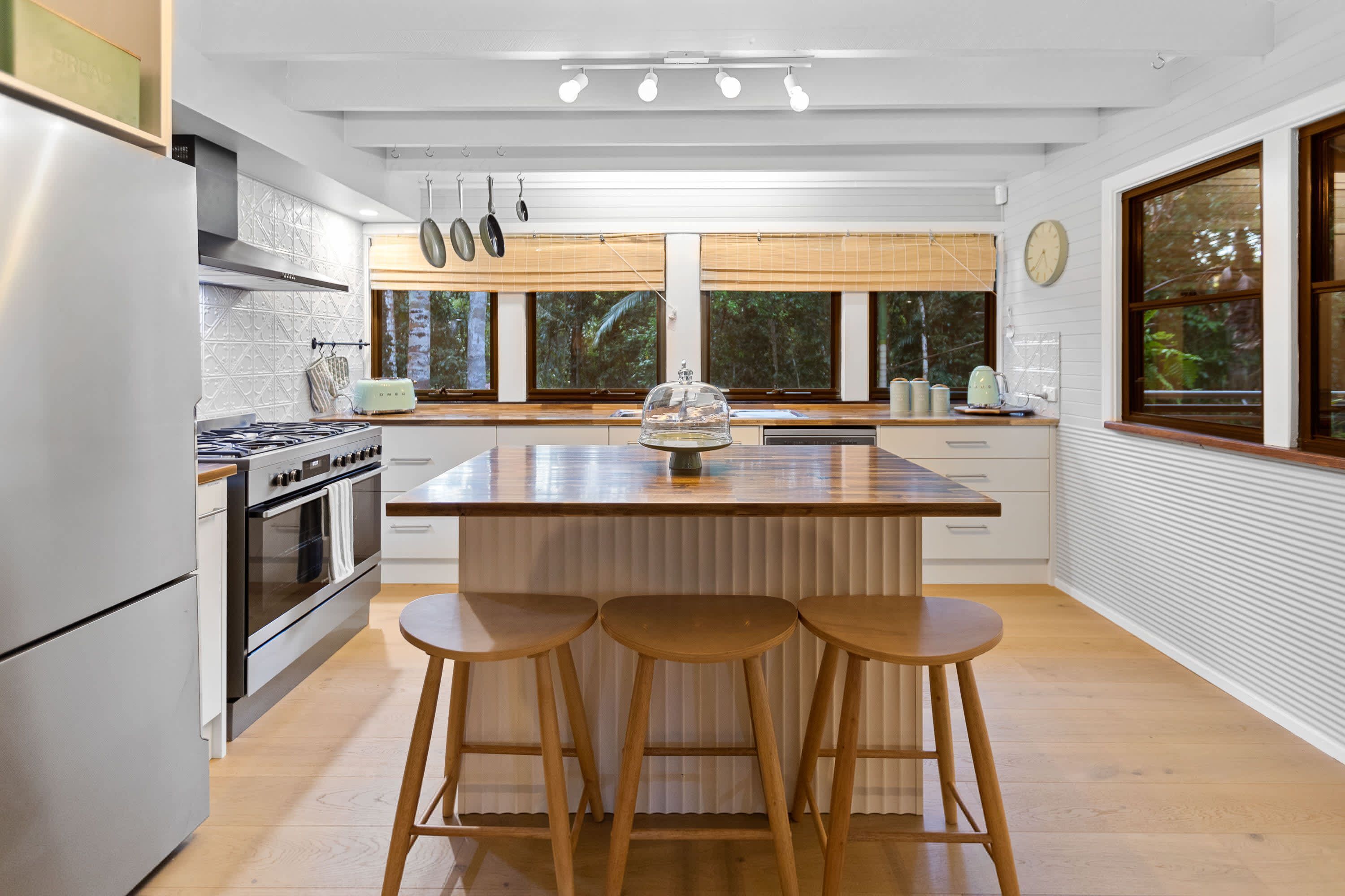 A modern kitchen with a central island, bar stools, stainless steel appliances, and large windows.