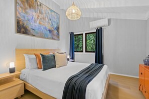 Um quarto com uma cama grande, uma mesa de cabeceira, um abajur, um quadro, uma janela com cortinas e um lustre.