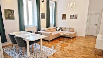 Ein modernes Wohnzimmer mit einer Couch, einem Esstisch, Stühlen, einem gemusterten Teppich und einer Chandelier.