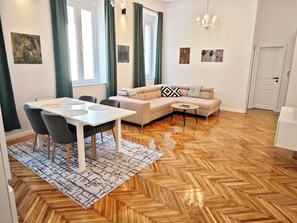 Ein modernes Wohnzimmer mit einer Couch, einem Esstisch, Stühlen, einem gemusterten Teppich und einer Chandelier.