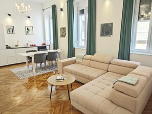 A modern living room with a beige sectional sofa, a round coffee table, and a dining area with a white table and chairs. - #Chic Harbor Old Town Bridge Apartment - TINELINN Apartments Zadar (Zadar)
