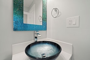 Ein Badezimmer mit einem weißen Waschbecken, einem Spiegel mit blauem Mosaikhintergrund und einem silbernen Wasserhahn.