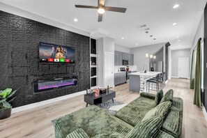 A modern living room with a flat-screen TV, a fireplace, and a sofa. - Modern 3BR Walk to Fair Park - EV Ready & Yard (Dallas)