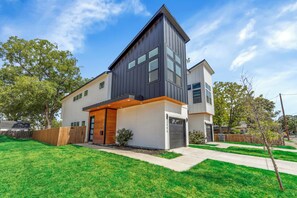 A modern two-story house with a flat roof, large windows, and a visible garage. - Modern 3BR Walk to Fair Park - EV Ready & Yard (Dallas)