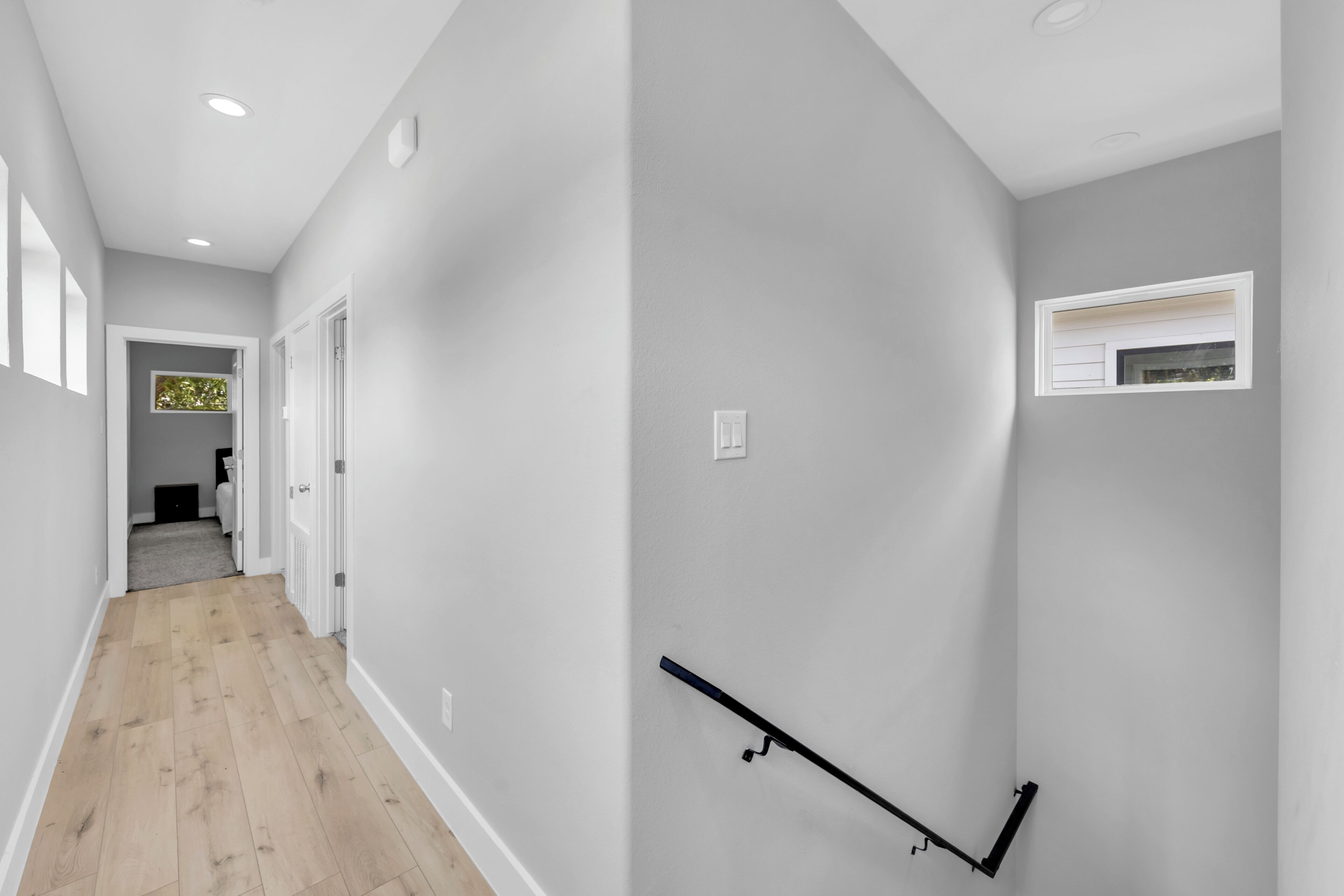 A hallway with a wooden floor, a white door, and a wall-mounted light fixture.
