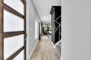 A hallway with a wooden floor, a door with frosted glass panels, and a black wall with white geometric patterns. - Modern 3BR Walk to Fair Park - EV Ready & Yard (Dallas)