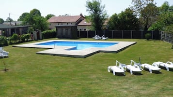 Un jardin avec une piscine rectangulaire, entourée d’une terrasse en bois, et un petit abri de jardin.