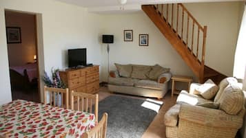 Un salon comprenant un canapé, un téléviseur, un escalier en bois et un coin repas avec une table.
